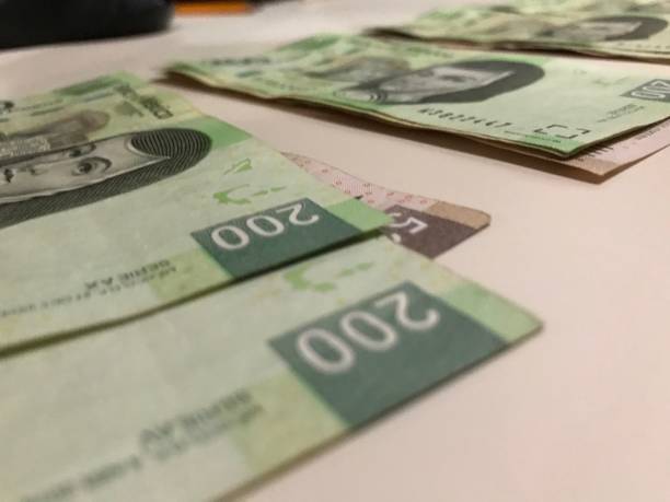 istock Some mexican pesos bills spread over a beige desk inside a small business office 1159488728