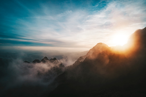 Amazing sunrise view from Mountains. sun sets behind the mountain. View from the top of a high mountain to valley covered with clouds. Silhouettes of mountain peaks in fog in bright sunlight.