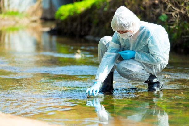 pesquisador cientista em terno de proteção leva água para análise de rio poluído - impurities - fotografias e filmes do acervo