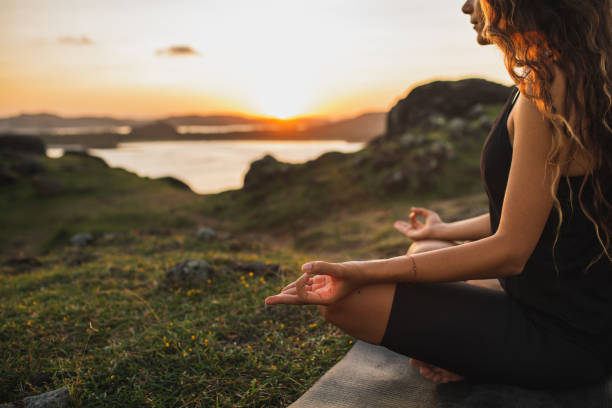 Healthy Lifestyle and Yoga Concept. Close-up hands. Woman do yoga outdoors at sunrise in lotus position. Woman exercising and meditating in morning. Nature background. stock photo