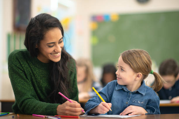 istock Beautiful teacher helps her student finish colouring her page 1159495582