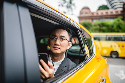 Portrait of Taiwanese business executive in taxi using smart phone and anticipating an important meeting.