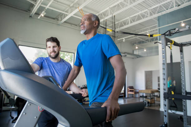 재활 약속 중 러닝 머신을 가진 노인 성인 남자를 돕는 물리 치료사 - treadmill 뉴스 사진 이미지