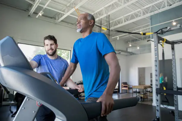 Physical therapist helping senior adult man with treadmill during rehabilitation appointment