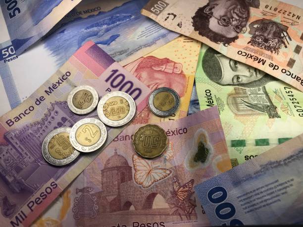 istock Many mixed Mexican peso bills spread over a wooden desk 1159498687