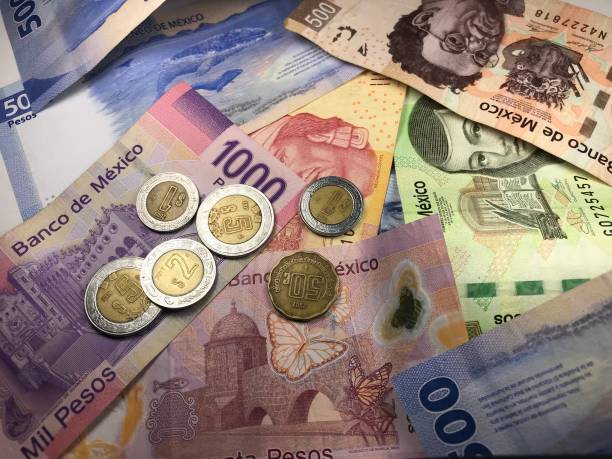 istock Many mixed Mexican peso bills spread over a wooden desk 1159498688