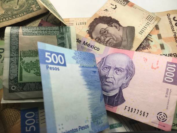 istock Many mixed Mexican peso bills spread over a wooden desk 1159498732