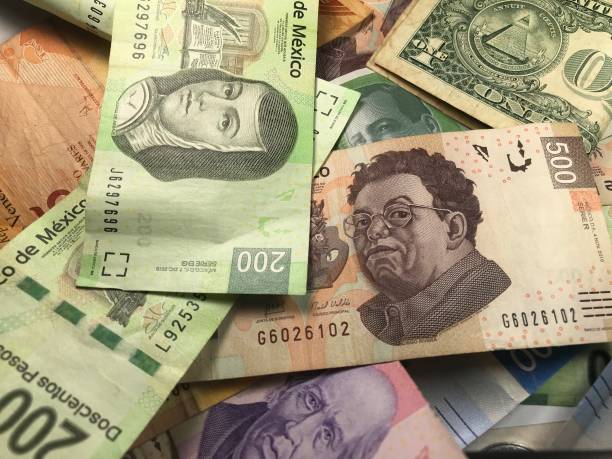 istock Many mixed Mexican peso bills spread over a wooden desk 1159498793