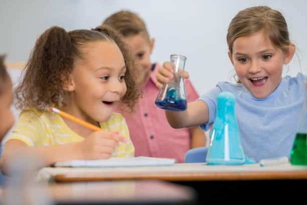 istock Cute little girls smile excitedly while doing science experiment in elementary STEM class 1159500417