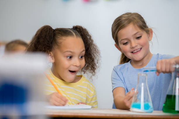 istock Cute little girls in science class smile excitedly while doing chemistry experiment 1159500478