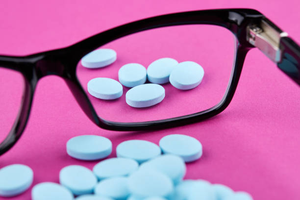 istock Glasses and blue pills on pink background. Medicine 1159502349