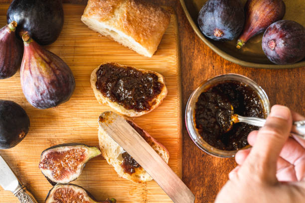 Fig Jam in a Jar,  Slice of Bread, and Fresh Figs on a Wooden Kitchen Table. Close Up, Top View, Woman Hands. Tasty Healthy Breakfast Concept, Still Life