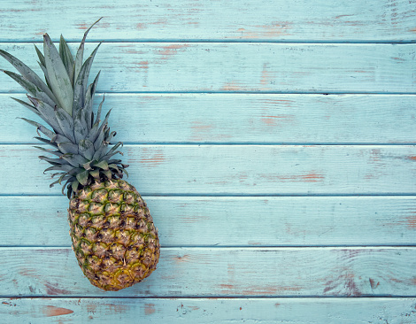 This is an overhead photograph of a pineapple on a wood light blue retro picnic bench. This image would work well in the summertime
