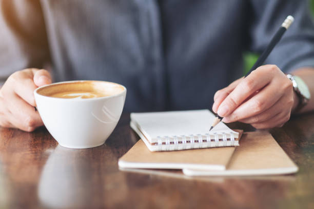 istock a woman writing on a notebook and holding a cup of coffee 1159508035