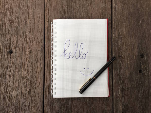 istock Hello text on notebook. Blank open notepad and black pen on old wood table background with copy space. Top view of open note book on grunge wood for business. Word Hello in notebook. 1159512697