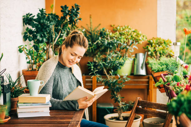 istock Young beautiful woman relaxing on cozy balcony, reading a book, wearing warm knitted pullover, cup of tea or coffee on stack of books 1159513989