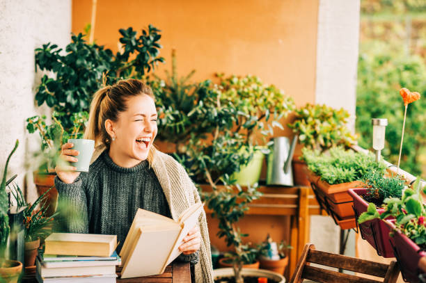 istock Young beautiful woman relaxing on cozy balcony, reading a book, wearing warm knitted pullover, holding cup of tea or coffee 1159513991