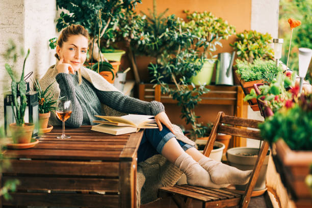 istock Young beautiful woman relaxing on cozy balcony, reading a book, wearing warm knitted pullover, glass of wine on wooden table 1159514005