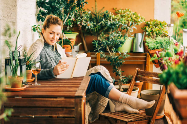 istock Young beautiful woman relaxing on cozy balcony, reading a book, wearing warm knitted pullover, glass of wine on wooden table 1159514044