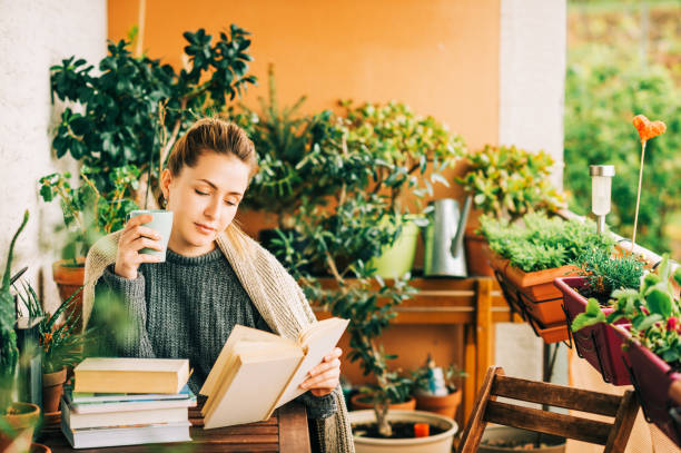 istock Young beautiful woman relaxing on cozy balcony, reading a book, wearing warm knitted pullover, holding cup of tea or coffee 1159514051