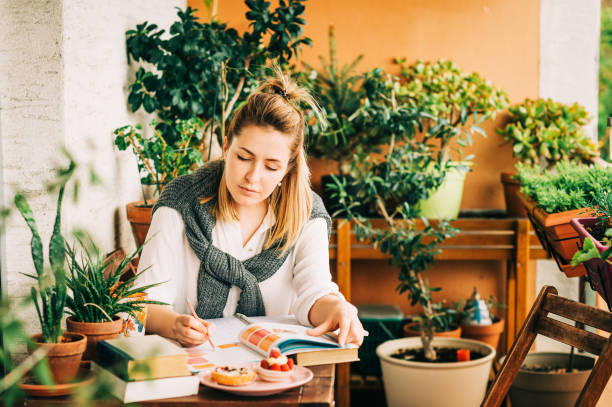 istock Young woman stuyding at home, sitting on the balcony, making notes in a nitebook 1159514052