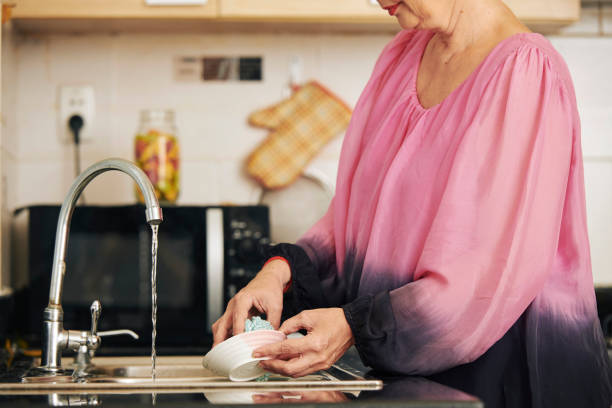 istock Woman rinsing plate under tap water 1159518820