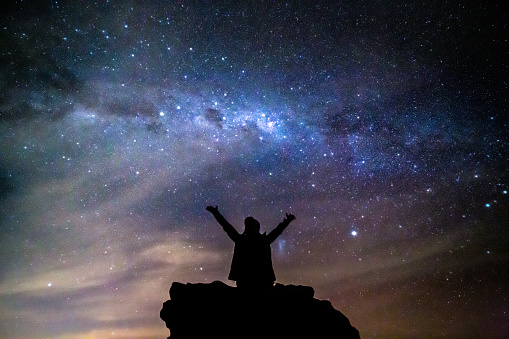 Woman arms outstretched to the starry cosmos above her