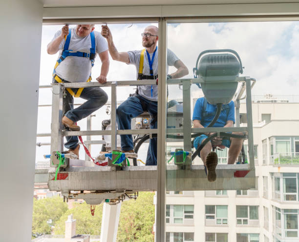 istock Team of blue-collar workers replacing a broken window in the office building - cleaning the frame after the old broken glass has been removed. High-altitude work on the lifting platform which is placed outside. 1159523587