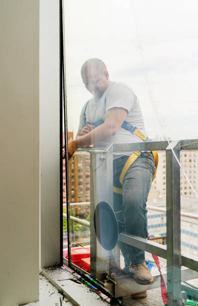 istock Team of blue-collar workers replacing a broken window in the office building - removing the old broken glass. High-altitude work on the lifting platform which is placed outside. 1159523632