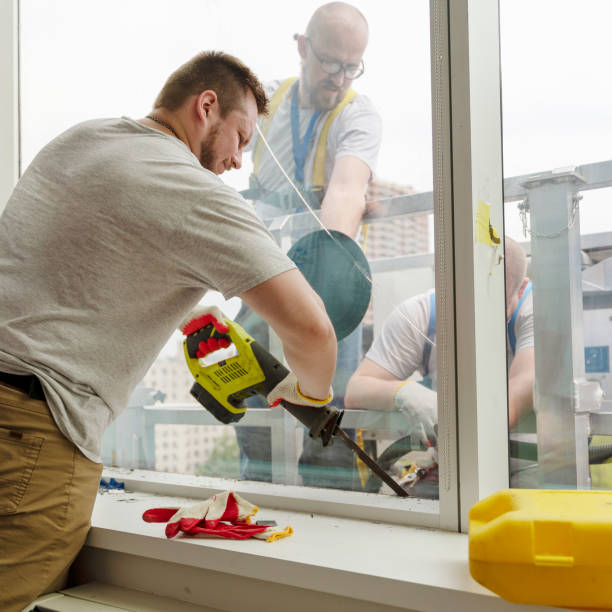istock Team of blue-collar workers replacing a broken window in the office building - removing the old broken glass. High-altitude work on the lifting platform which is placed outside. 1159523640