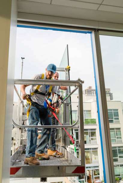 istock Team of blue-collar workers replacing a broken window in the office building - applying a fresh sealant for a new glass installation. High-altitude work on the lifting platform which is placed outside. 1159530186