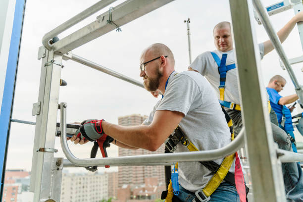 istock Team of blue-collar workers replacing a broken window in the office building - applying a fresh sealant for a new glass installation. High-altitude work on the lifting platform which is placed outside. 1159530189