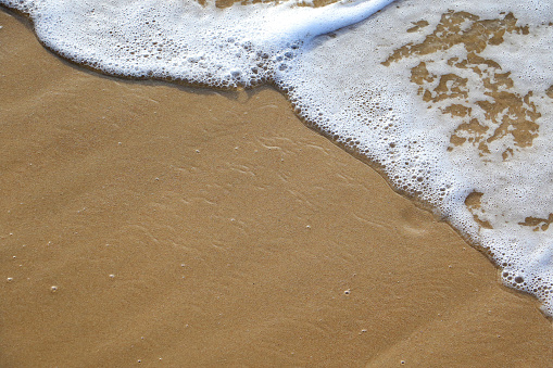 tranquil waves washing up sandy brown beach forming bubble and foam with space for text