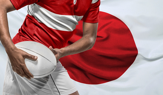 Male african rugby player with a ball in front of a Japanese flag