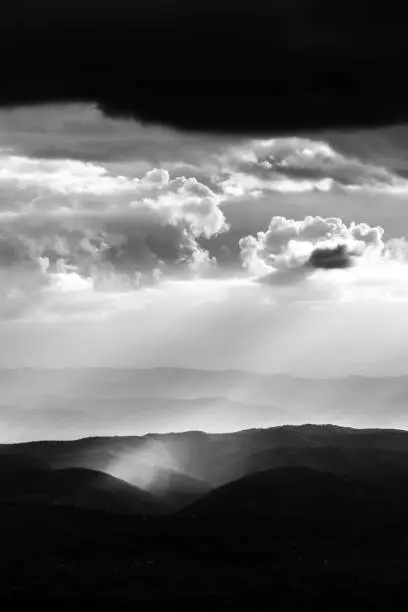 Sunray shines through clouds over the mountains in the middle of shadows.