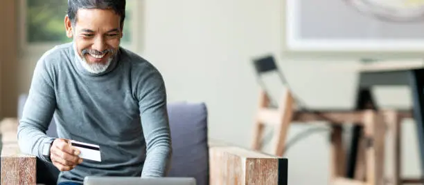 Photo of Attractive bearded hipster asian father or Hispanic old man using Laptop and credit card payment shopping online with customer network connection via omni channel system. Older man with technology.