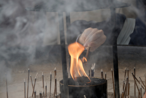 Close-up of a hand lighting an incense stick at a Buddhist temple.