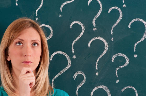 istock Pensive Woman in front of Question Marks Sketched on Blackboard 1159546516