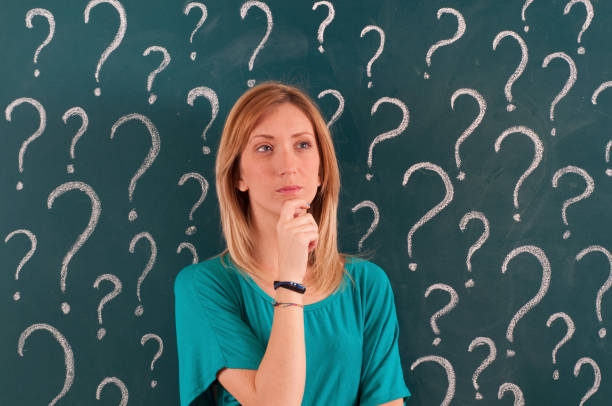 istock Pensive Woman in front of Question Marks Sketched on Blackboard 1159546519