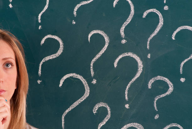 istock Pensive Woman in front of Question Marks Sketched on Blackboard 1159546521