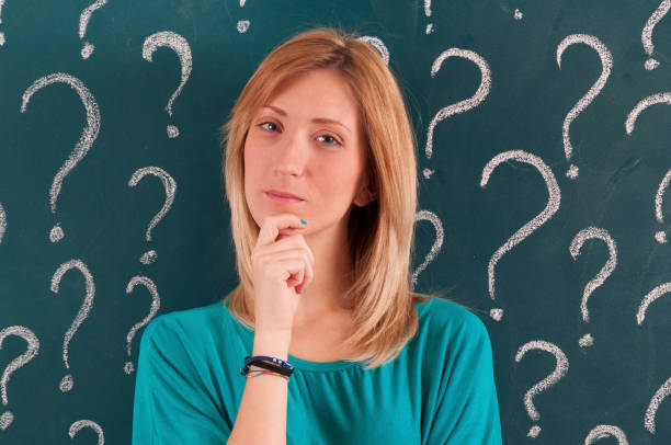 istock Pensive Woman in front of Question Marks Sketched on Blackboard 1159546529