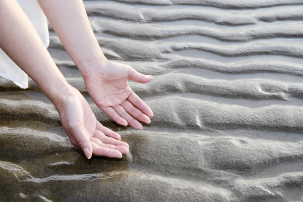 Two hands are laying on the sand, one of which is wearing a ring. The other hand is bare