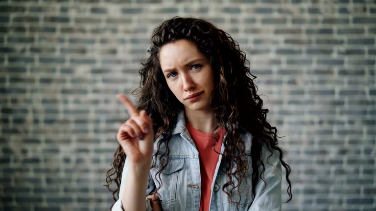 Portrait of strict girl waving finger shaking head meaning no near brick wall