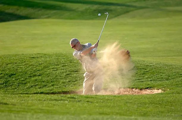 a golfer blasts his ball from the sand trap