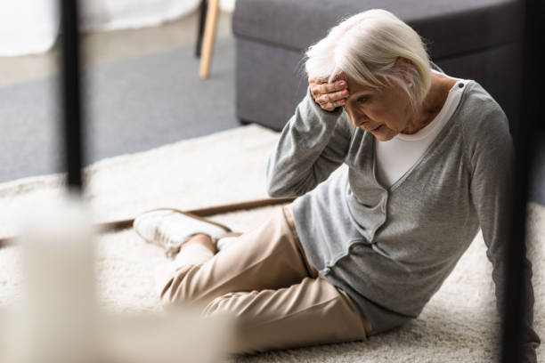 seniorin mit migräne auf teppich sitzend und berührende stirn mit der hand - schwindelig stock-fotos und bilder