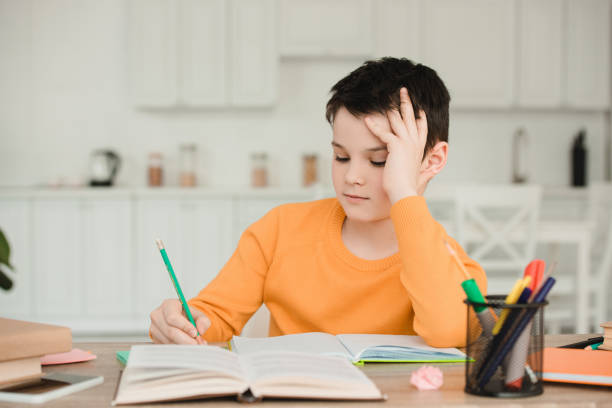 istock attentive schoolboy reading book and writing while doing schoolwork at home 1159555419
