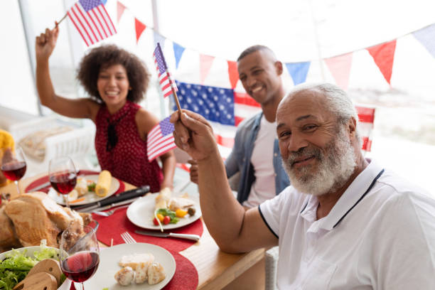 Family celebrating US Independence day on a dining table Side view of Multi-generation African American family celebrating US Independence day on a dining table at home patriotic man stock pictures, royalty-free photos & images