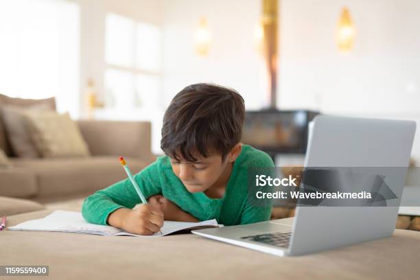 Boy Using Laptop While Drawing A Sketch On Book At Home Stock Photo - Download Image Now