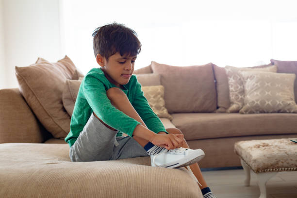 Boy tying shoelace on sofa in living room at comfortable home stock photo