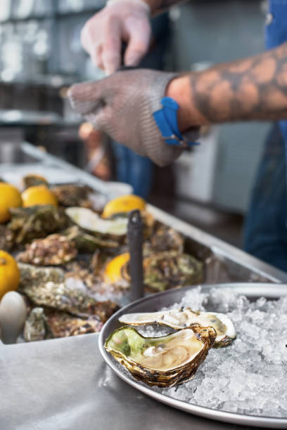 シェフは、ナイフとステンレススチールメッシュオイスターグローブで新鮮な牡蠣をシャッキング。 - prepared oysters prepared shellfish shucked seafood ストックフォトと画像